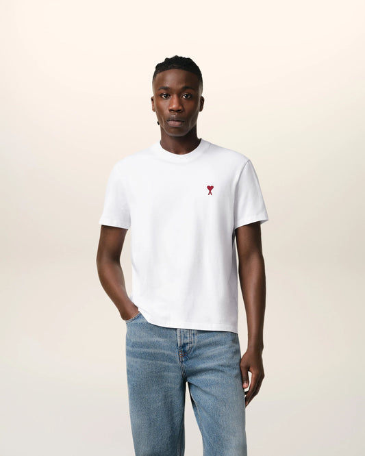 Person wearing a white t-shirt with a small red logo on a plain background