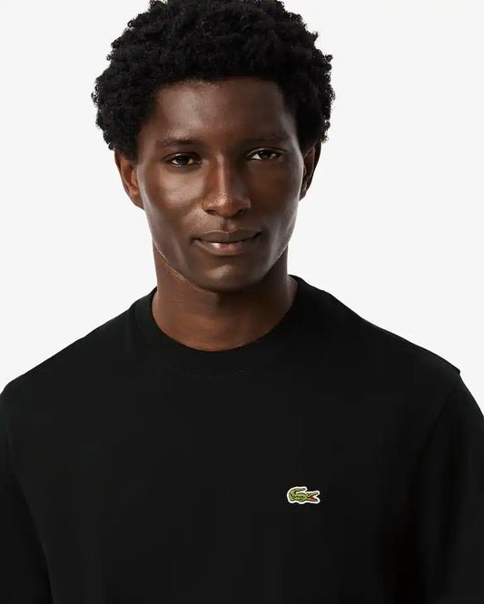 Person wearing a black Lacoste shirt with a green logo on a white background