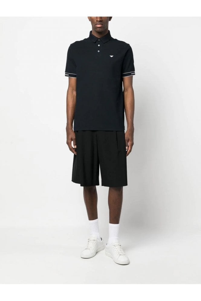 Person wearing a black polo shirt and shorts with white sneakers on a white background