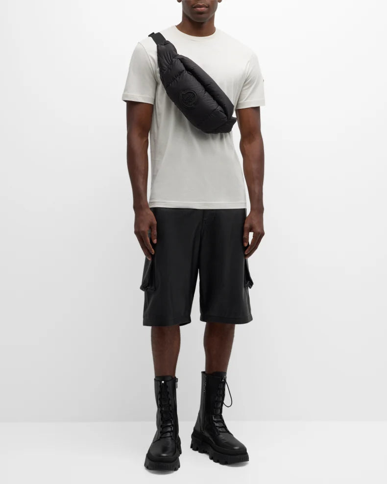Person wearing a white t-shirt, black cargo shorts, and black boots with a black bag over one shoulder on a white background.