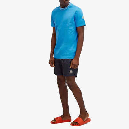 Person wearing a blue t-shirt and dark shorts with orange sandals on a white background