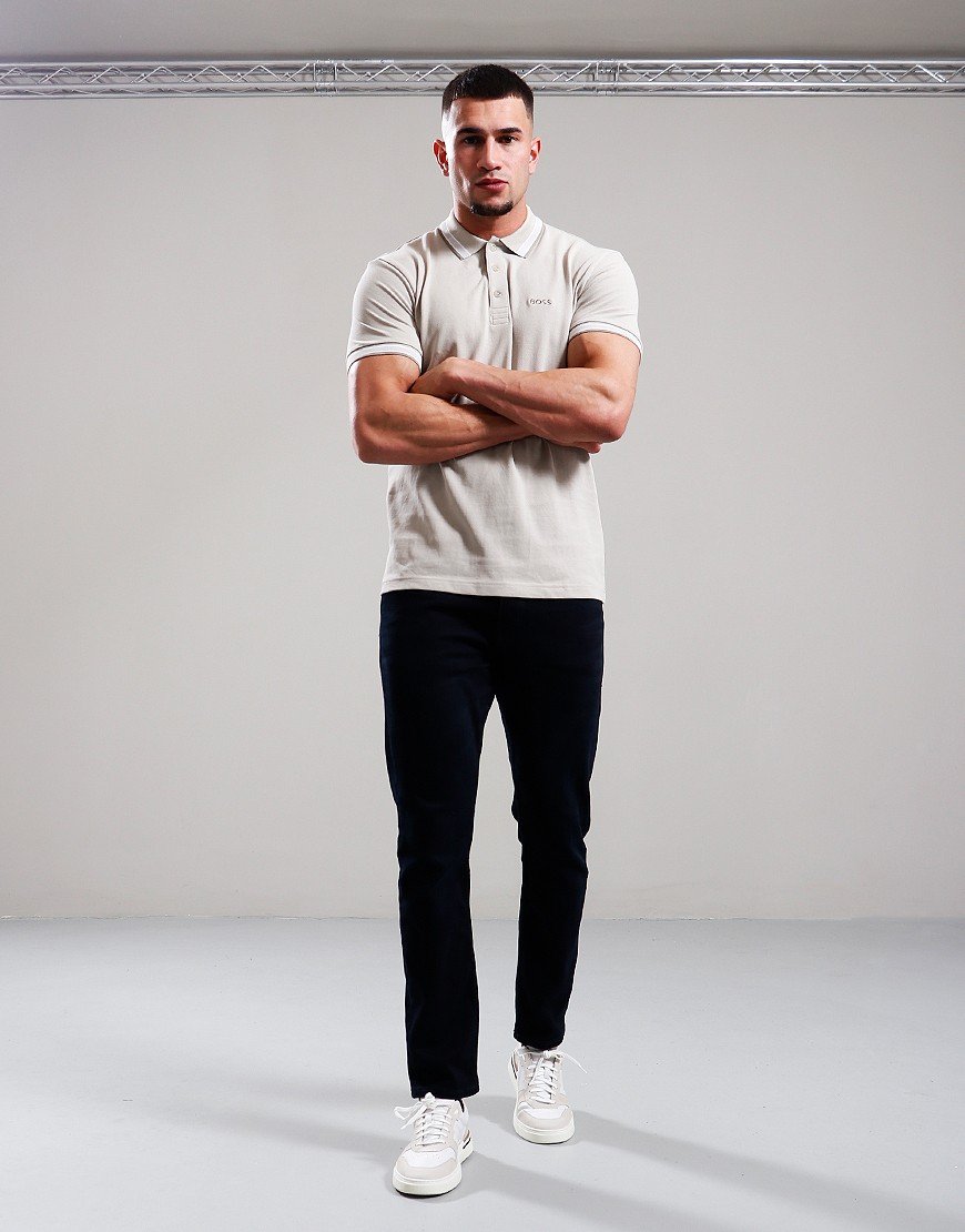 Man wearing a white polo shirt, black pants, and white sneakers against a plain background