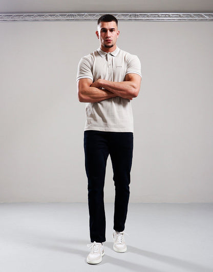Man wearing a white polo shirt, black pants, and white sneakers against a plain background