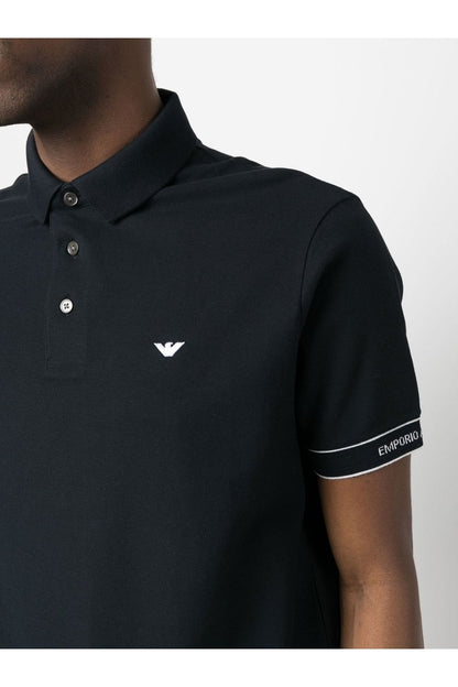 Black polo shirt with a logo on the chest and brand name on the sleeve, worn by a person.