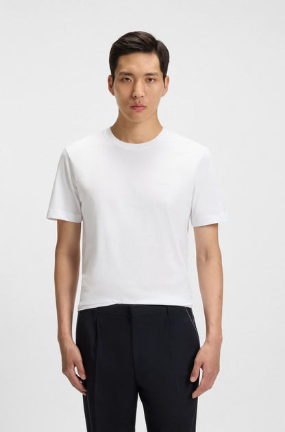 Man wearing a plain white t-shirt and black pants on a light gray background