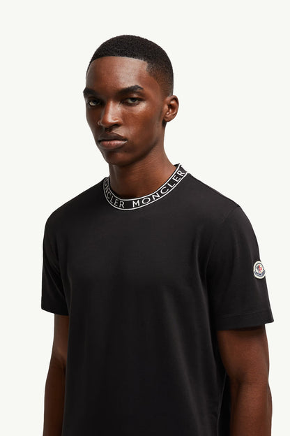 Man wearing a black t-shirt with a brand logo on a white background