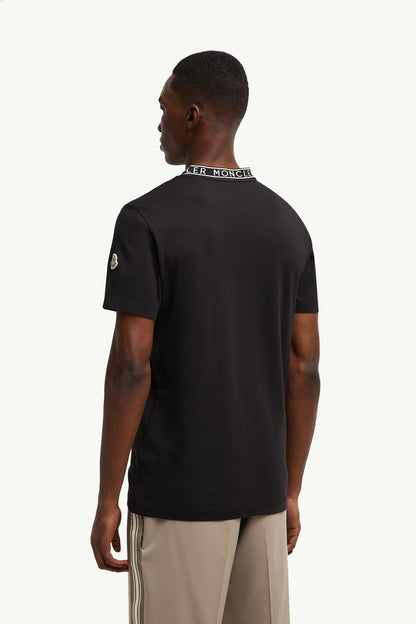 Man wearing a black t-shirt with visible branding on the back, standing against a white background