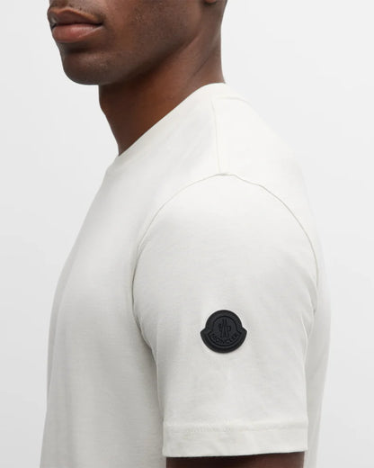 White t-shirt with a black logo on the sleeve against a light gray background